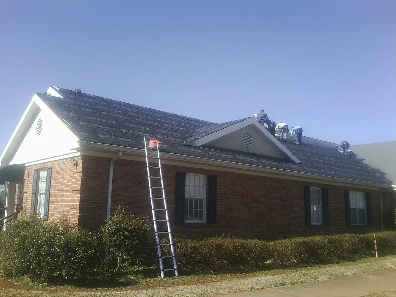 Crew tearing shingles off a brick ranch roof with a ladder set — Metal Roof Repair work by our crew in Wilsonville