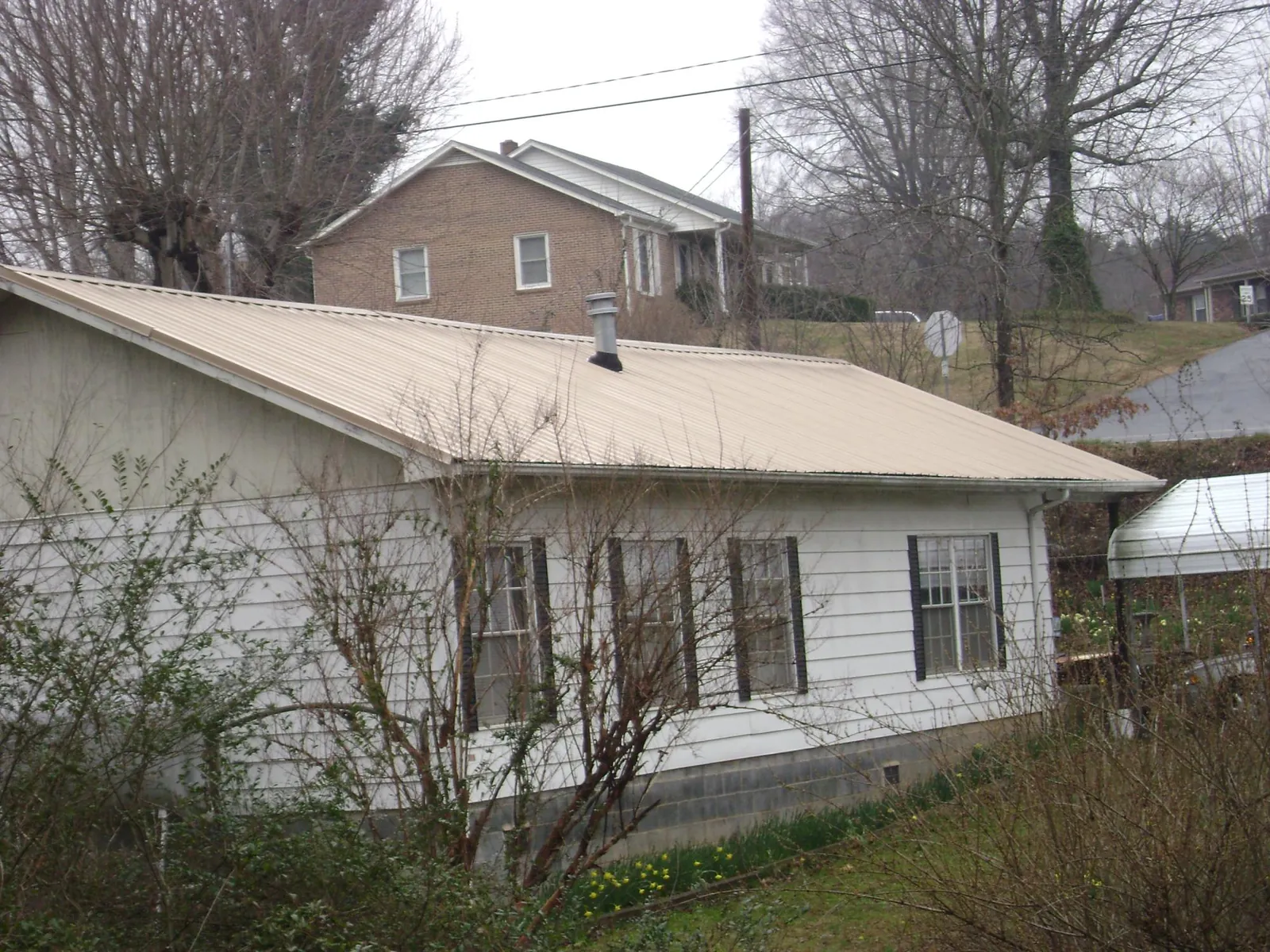 Tan metal roof on a white sided house set into a hillside — Commercial Roofing by Roofing Brothers in Wilsonville